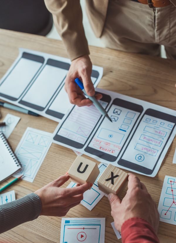 Web designers holding up two wooden blocks spelling "UX" and designing a mobile user interface